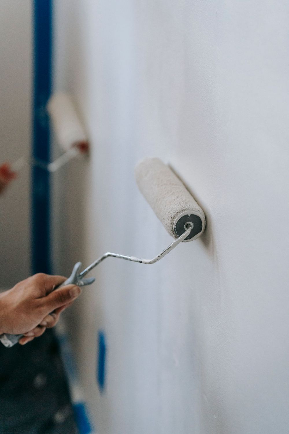 Hand met een verfroller tegen een witte muur